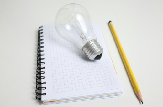 Un cuaderno de escritura, una bombilla y un lápiz. foto de Cht Gsml en Unsplash.